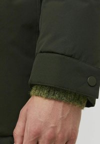 Dark green padded jacket cuff with a contrasting fuzzy green knit interior and metal snap closure. Visible stitching along the edge.