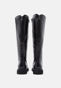 Pár čiernych kožených čižiem po kolená s zadnými zipsami a hrubými podrážkami, zobrazený zozadu na bielom pozadí.