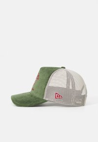 Gorra de pana verde con malla en la parte posterior, que presenta bordados rojos en la parte frontal y un pequeño acento de logotipo rojo en un lado. Diseño de visera plana.