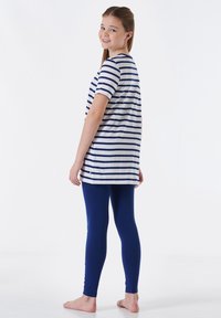 Koszulka w paski z krótkim rękawem w kolorze białym i granatowym, zestawiona z dopasowanymi granatowymi legginsami. Koszulka ma nieco dłuższy tylny dół. Na bosaka.