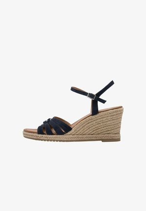 Navy blue suede wedge sandals with crisscross straps and a buckled ankle strap. Rope-stitched wedge heel and smooth brown insole.