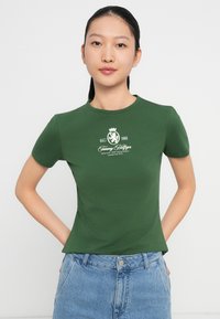 Camiseta verde ajustada de algodón con cuello redondo y manga corta, que presenta una impresión de logo blanco en la zona del pecho.