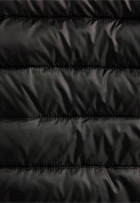 Černá tkanina provatované bundy s hladkým povrchem a horizontální prošívanou stehovou výšivkou. Povrch jemně odráží světlo.