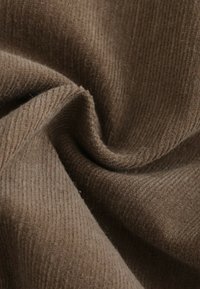Tissu en velours côtelé brun avec une texture douce et des nervures verticales proéminentes, créant une surface chaude et durable.