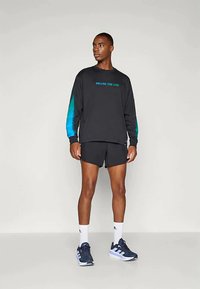 Black long-sleeve shirt with gradient blue sleeves and "FOLLOW THE LINE" text, paired with black shorts and blue athletic shoes.