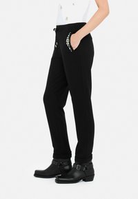 Sorte sweatpants med snoreliv og dekorative nitter på den forreste lomme, parret med sorte ankelstøvler.