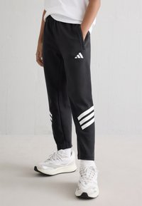 Melni sporty apstākļi ar brīvu piegriezumu, kas rotāti ar baltu Adidas logo un trīskārtēju svītru apakšējā daļā. Izgatavoti no mīksta auduma, ar sānu kabatām.