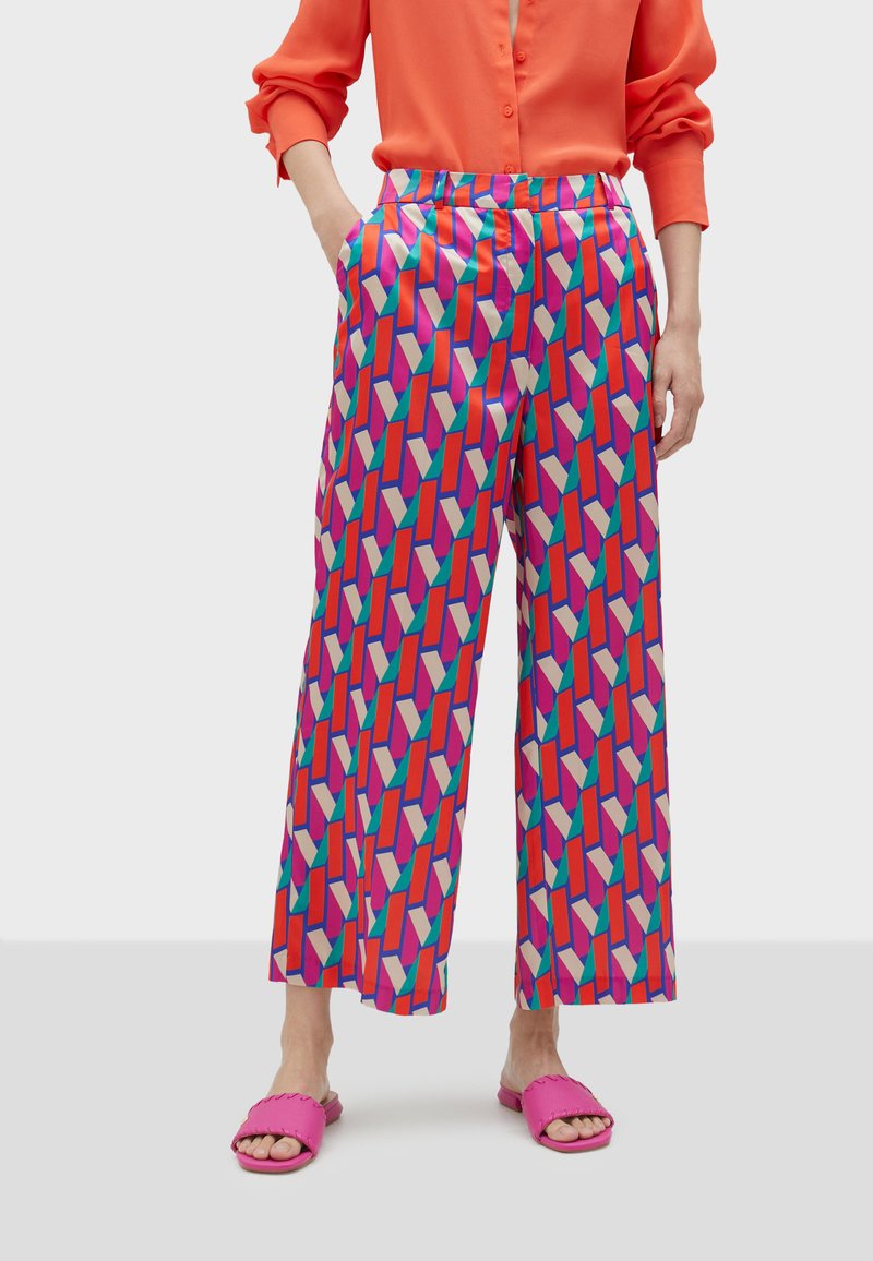 Färgglada, vida byxor i slät tyg med ett djärvt geometriskt mönster i rosa, rött, grönt och krämfärgade nyanser.