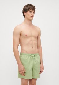 Heledad rohelised ujumispüksid, mis on valmistatud pehmest kangast, elastse vöökoha ja nööriga, ulatudes veidi üle reie keskmise osa.