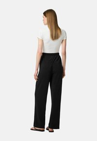 Pantalons larges noirs en tissu texturé, avec une taille élastique. Le haut est un tee-shirt blanc ajusté à manches courtes.