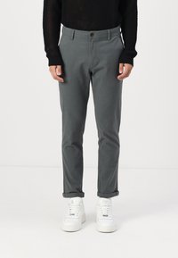 Grå bomullsbukser med slim fit, med knappeåpning og oppbrettede ermer, kombinert med hvite sneakers. Strikket genser med tekstur over.
