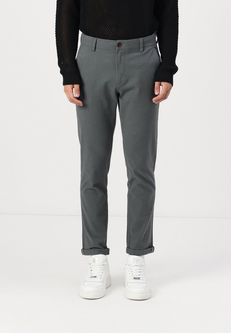 Grå bomullsbukser med slim fit, med knappeåpning og oppbrettede ermer, kombinert med hvite sneakers. Strikket genser med tekstur over.