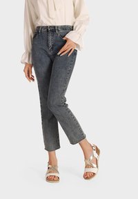 Jeans di denim blu scuro con una vestibilità slim e orlo sfrangiato, abbinati a sandali beige con cinturini incrociati e suola a zeppa.