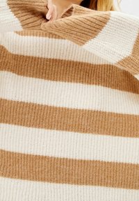Sweter w paski z dużymi beżowymi i białymi naprzemiennymi pasami, charakteryzujący się dzianinową teksturą i luźnym krojem.