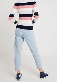 Sweter w pasy w kolorach różowym, granatowym i białym; prążkowana tekstura. Jasnoniebieskie dżinsy, lekko zwężane z tylnymi kieszeniami. Granatowe sneakersy.