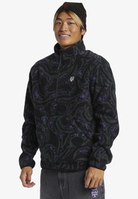 Schwarzer Fleecepullover mit spiralförmigen grünen und lila Mustern, halber Reißverschluss vorne, Stehkragen und Kängurutasche. Mit Logo auf der Brust.