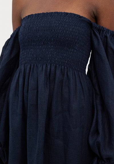 Marine off-shoulder kjole med smocket liv og voluminøse ermer, laget av lett stoff med myk tekstur.