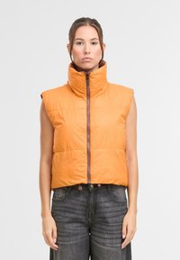 Oranžová bezrukávová prešívaná vesta s vysokým golierom, predným zipsom a dvoma patentkami na spodnom okraji. Hladká textúra, izolovaný dizajn.