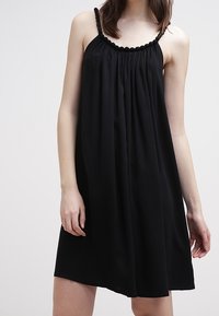 Black slip dress with pleated bodice, thin straps, and a textured, gathered neckline, made from a lightweight, flowing fabric.