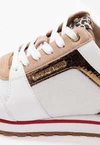 Weiße Sneakers mit tanfarbenen Wildlederelementen, goldenen Metallakzenten und Leopardenmuster. Sie verfügen über weiße Schnürsenkel und eine strukturierte Oberfläche. Rote Sohlenstreifen.