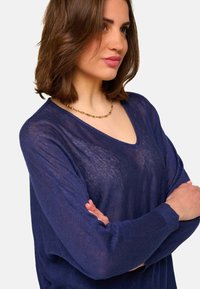 Pull léger en maille bleu marine avec un col en V et des manches longues. Doté d'une coupe décontractée et de bords côtelés. Texture douce avec une légère transparence.