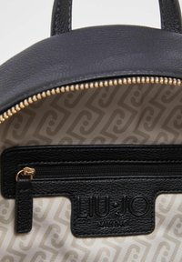 Intérieur d'un sac en cuir noir texturé avec une fermeture éclair dorée, une étiquette de marque et une doublure en tissu beige à motif subtil.