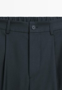 Dunkelgraue Hosen aus gewebtem Stoff, mit Knopfverschluss, plissiertem Vorderteil und einem elastischen Bund für Komfort.