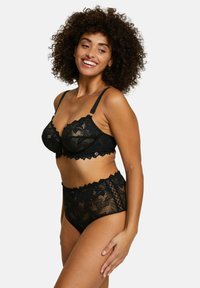 Set di lingerie in pizzo nero con reggiseno balconcino dai bordi ondulati e culotte a vita alta con intricate fantasie floreali e dettagli a intaglio.