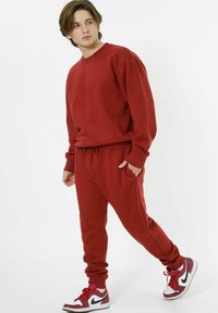 Roter Kapuzenpullover und passende Jogginghose aus weichstoff; mit gerippten Bündchen, verstellbarem Bund und Seitentaschen; kombiniert mit roten und weißen Sneakers.