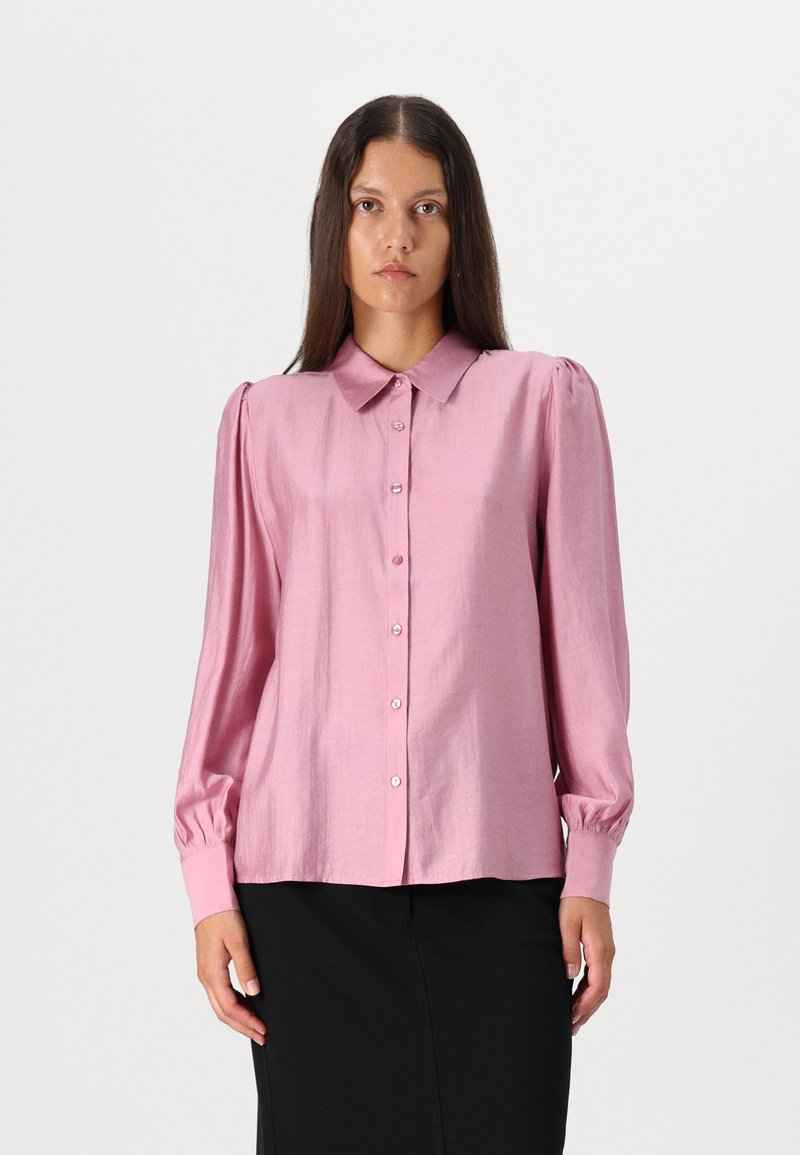Camisa rosa com botões, colarinho, mangas longas e ombros bufantes; feita de um tecido brilhante com pequenos botões e uma textura suave.