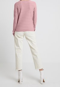 Maglione a strisce rosa con maniche lunghe, abbinato a pantaloni bianchi a vita alta con gamba dritta. Stivaletti bianchi alla caviglia con tacco spesso.
