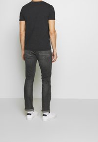Camiseta gris oscuro de manga corta, combinada con jeans de mezclilla oscuros. Zapatillas blancas con acentos negros y puños enrollados. Diseño minimalista.