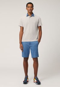 Svijetlosiva polo majica s traper ovratnikom, uparena sa svijetloplavim traper kratkim hlačama. Model nosi šarene sportske tenisice.