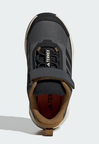 Chaussure de sport noire et grise avec une tige texturée, un support de cheville rembourré, une sangle ajustable et des détails intérieurs orange.