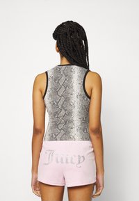 Femme aux longs cheveux tressés portant un débardeur imprimé serpent et un short rose avec le texte "Juicy" en strass dans le dos.