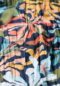 Tissu à motifs floraux dans plusieurs couleurs, y compris marine, vert et corail. Présente une surface texturée avec des détails de plis tout au long.