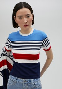 Randig stickad topp med blå, röd, vit och marinblå färg. Korta ärmar, rund halsringning och en figursydd design. Slät textur.