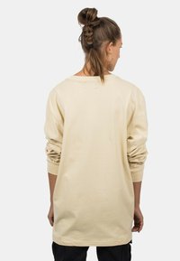 Beige Langarmshirt mit lockerer Passform, runden Ausschnitt und hochgekrempelten Ärmeln, aus weichem Baumwollstoff. Details umfassen einen geraden Saum.