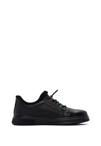 Sneaker nera a basso con pannelli laterali texturizzati, lacci neri, occhiello rosso e suola in gomma spessa su uno sfondo bianco.