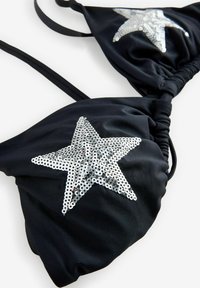 Čierny bikini top so zakrývajúcimi striebornými hviezdami, ktorý má nastaviteľné ramienka a zložený dizajn. Mäkký, elastický textil.