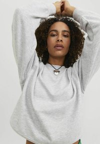 Gai pelēks pārspīlēts džemperis ar ribotām piedurknēm un apakšmalu, ar noapaļotu kakla izgriezumu un mīkstu tekstūru. Uzvalkots sudraba sirds auskars.