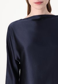 Marine satintopp med bred halslinning og lange ermer, med en jevn tekstur og subtil glans. Ingen trykk eller dekorasjoner synlige.