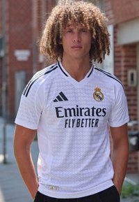 Maglia bianca Adidas con accenti neri, con il testo "Emirates Fly Better" e il logo del Real Madrid. Vestibilità atletica con un design testurizzato.