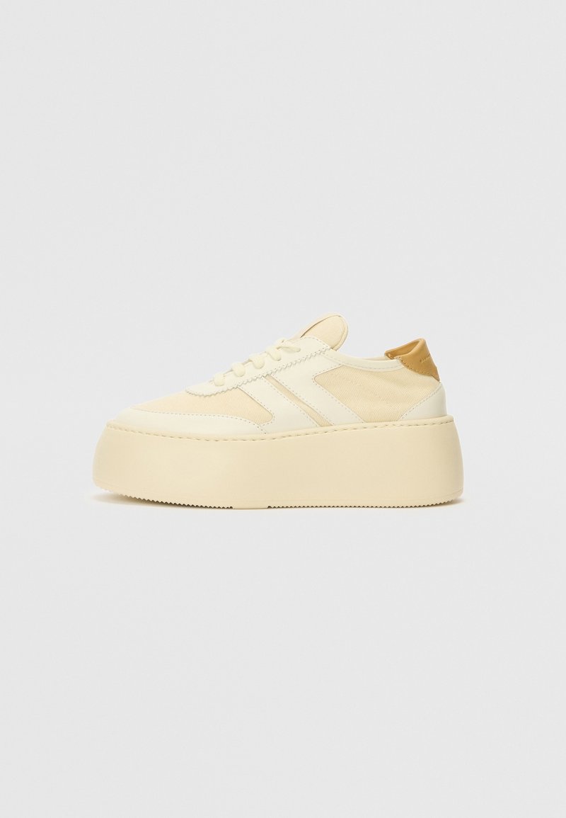 Platform sneakers made of light beige synthetic material. Features a rounded toe, lace-up front, and a contrasting beige heel accent.