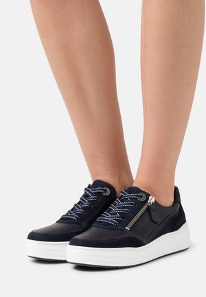 Baskets bleu foncé avec une tige texturée, une semelle plateforme blanche, des lacets contrastés et un accent zippé sur le côté.