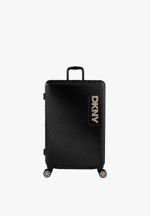 Maleta rígida negra con surcos diagonales, asa retráctil y cuatro ruedas. Presenta un logo dorado de DKNY en el bolsillo lateral.