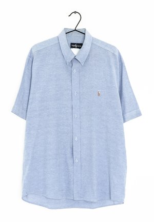 Camisa de manga corta azul claro con botones y cuello, con el logo de Ralph Lauren bordado en el pecho, colgada en una percha negra.