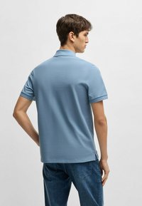 Ljusblå pikétröja med korta ärmar, platt krage och sidofickor, i kombination med mörka jeans. Slät, texturerad tyg.