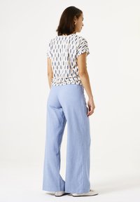 T-Shirt mit kurzen Ärmeln im Muster in Creme und Blau, kombiniert mit hellblauen, weit geschnittenen Hosen. Weicher Stoff mit lockerer Passform und einfachem Design.