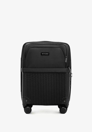 Maleta negra con diseño acanalado en la mitad inferior, bolsillos con cremallera en la parte superior y cuatro ruedas para movilidad. Marcada "Wittchen."